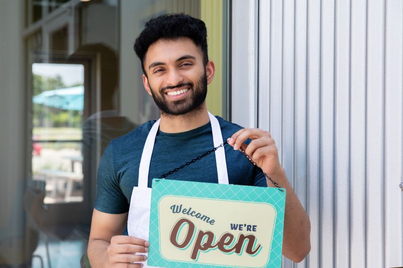 Man holing a now open sign for his new business